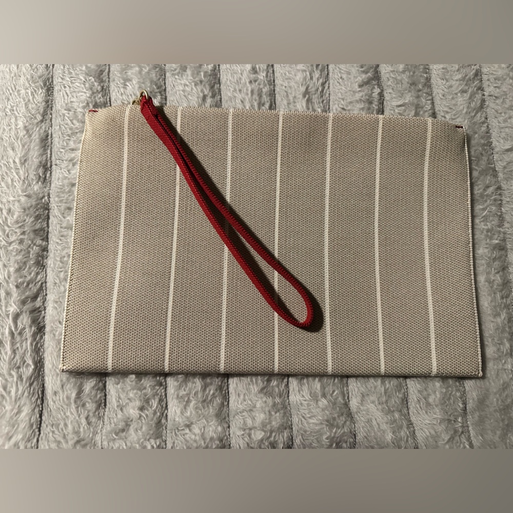 Rothy’s The Wristlet Clutch in Beige and White with red wristband accent.